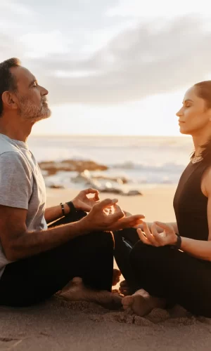 A couple meditating at the beach seashore.